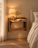 Walnut-tone fold-down wall-mounted bedside cabinet fixed to the wall with a lamp switched on and an open book in the evening