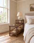 Walnut three-tier step bedside table beside a linen bed in a British bedroom with a sash window