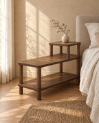 Three-quarter view of the walnut step bedside table showing its round legs and bottom shelf