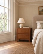 Walnut-tone wooden bedside table with 2 drawers beside a linen bed in a bright British bedroom with a sash window