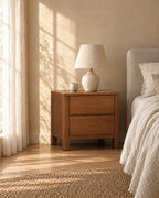 Walnut-tone wooden bedside table with 2 drawers in warm morning light with window shadows on the wall
