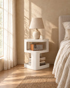 White sculpted bedside table with a ceramic lamp in morning light
