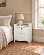 White bedside table with a lockable drawer beside a linen bed in a British bedroom with a sash window