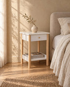 Three-quarter view of the white bedside table showing its pine legs and lower shelf
