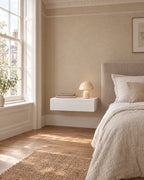 White floating bedside table beside a linen bed in a bright British bedroom with a sash window