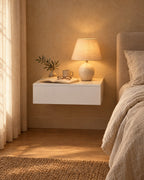 White floating bedside table with a lamp switched on and an open book in the evening
