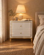 White and gold bedside table, lamp switched on and an open book in the evening