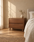 Wide walnut-effect bedside table standing beside a bed with linen bedding